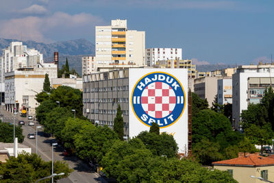 Road sign by buildings in city against sky