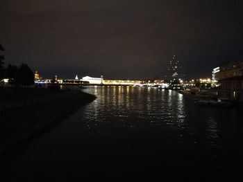 Illuminated city by sea against sky at night