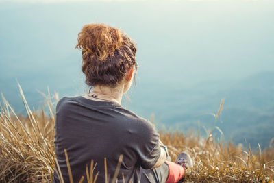 Rear view of hiker sitting on cliff against sky