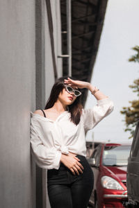 Young woman wearing sunglasses standing against car