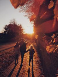 Rear view of people walking on footpath against sky during sunset