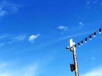 Low angle view of pole with security camera and lighting equipment against blue sky