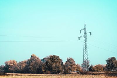 Low angle view of electricity pylon on field against clear sky