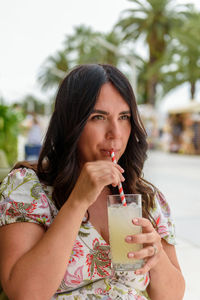 Pretty girl with long hair sitting in bar outdoor in city, drinking lemonade on straw
