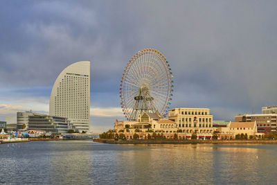 Illuminated ferris wheel by buildings against sky