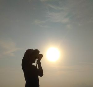 Side view of silhouette man photographing against sky during sunset