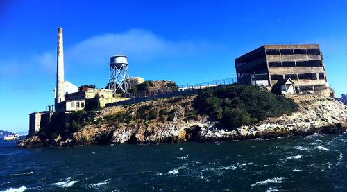 Water tower by sea against clear blue sky