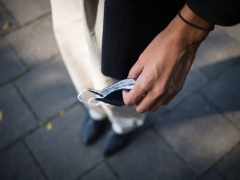 Low section of person holding mask while standing on footpath