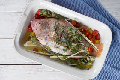 Raw red tilapia fish cooked with herbs, spices, paprika and tomatoes, lemon,