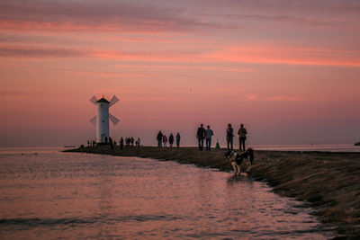 Silhouette people by sea against sky during sunset