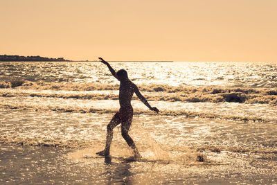 Silhouette young man with arms raised at beach against sky during sunset