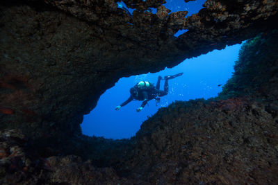 Man scuba diving amidst rocks in sea