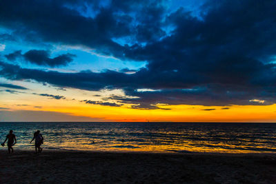 Silhouette people on beach against sky during sunset