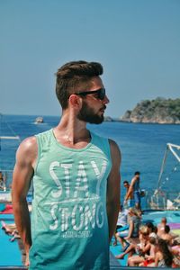 Handsome man standing at beach against clear blue sky