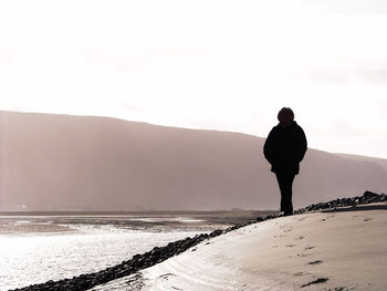 Silhouette woman standing on sand against mountain at mawddach estuary