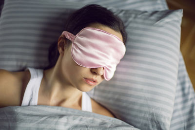 Woman in a pink eye mask lies under a blanket in a bed and suffers from insomnia