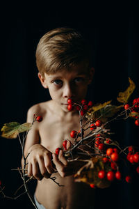 Portrait of boy holding berries against black background