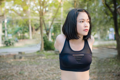 Young woman looking away while standing against trees