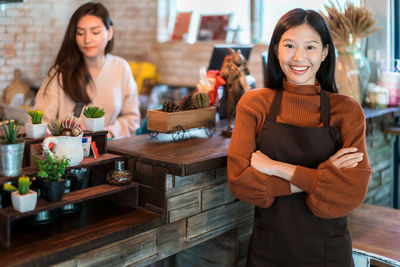 Portrait of smiling barista with arms crossed standing in cafe