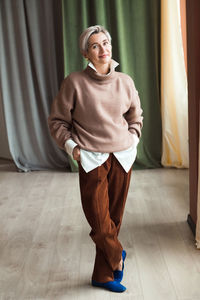 Fashion woman in brown oversize sweater and trousers standing in modern work place or office