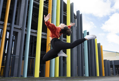 Portrait of beautiful brunette jumping in front of colorful building