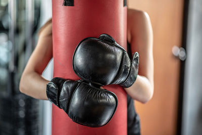 Midsection of woman embracing punching bag in gym