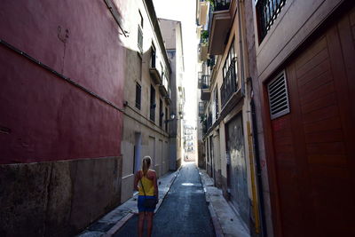 Rear view of man walking on narrow street amidst buildings