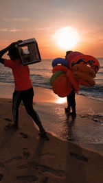 Men on beach against sky during sunset