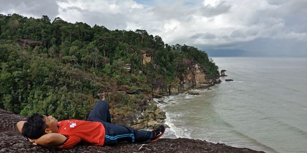 Man lying on cliff against sea