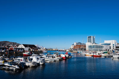Boats moored in sea by buildings against clear blue sky