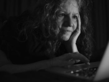 Close-up of thoughtful senior woman using laptop in darkroom