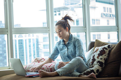 Young woman using mobile phone while sitting on sofa