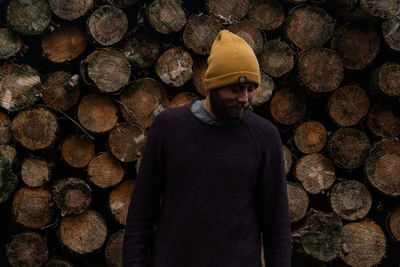 Male in winter clothes standing before a pile of logs freshly cut.