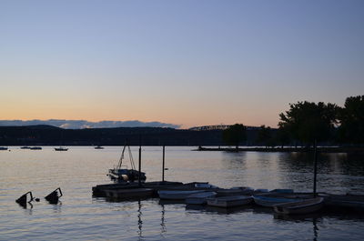 Silhouette boats moored in lake against clear sky