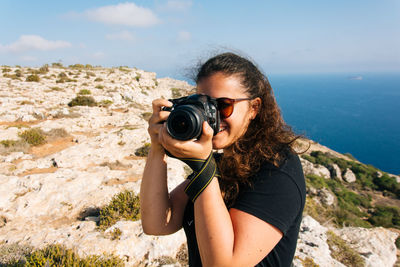 Young woman photographing on cliff against sky