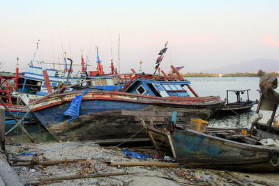 Fishing boats moored at shore against sky during sunset