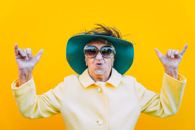 Portrait of senior woman gesturing against yellow background