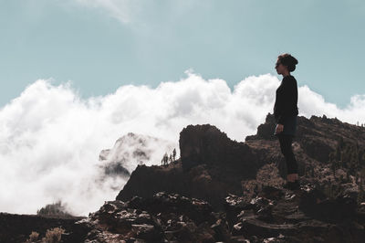 Side view of woman standing on rock against cloudy sky