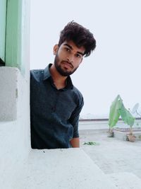 Portrait of young man sitting against wall