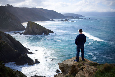 Rear view of man standing on rock over sea