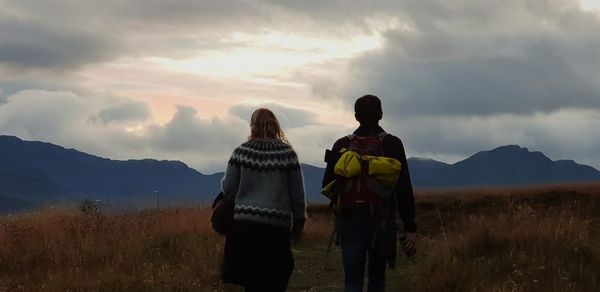 Rear view of couple walking on field against sky