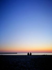 Silhouette people on beach against clear sky during sunset