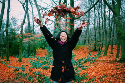 Smiling young woman standing by tree in forest