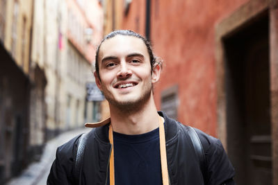 Close-up portrait of smiling young man against buildings in alley