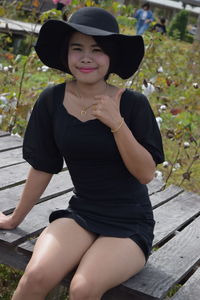 Portrait of young woman gesturing thumbs up sign while sitting on boardwalk