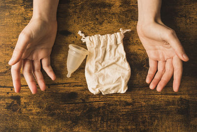 Woman with menstrual cup and cloth bag on wooden table