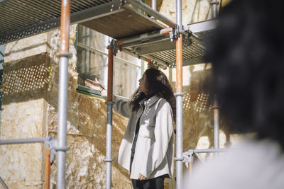 Female architect talking to client while standing under scaffolding at under construction apartment