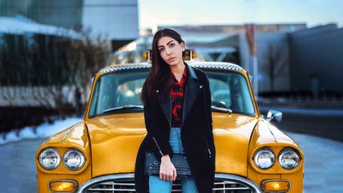 Portrait of young woman standing by yellow car