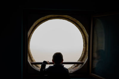 Rear view of boy looking at sea through window