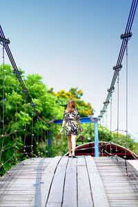 Rear view of woman standing on footbridge against clear sky